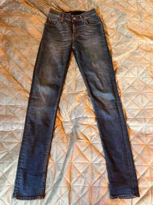 Blå jeans från tiger of sweden - Säljer ett par blå jeans från tiger of sweden med klassisk femficksdesign och läderpatch bak i midjan. Jeansen har en snygg tvätt med lätt slitning och är tillverkade i stretchigt denim för en bekväm passform.
