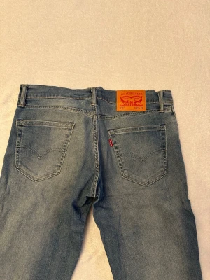 Levi's ljusblå jeans med klassisk passform - Ljusblå jeans från Levi's med klassisk femficksdesign och snygga slitningar på framsidan. Jeansens bakfickor har den ikoniska Levi's-sömmen och ett brunt läderpatch med logotyp. Materialet är denim och modellen har raka ben. Oanvända! Nypris ca 1400kr