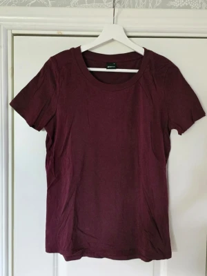 Vinröd t-shirt från Gina Tricot - En enkel och stilren vinröd t-shirt från Gina Tricot. Tillverkad i mjuk och hållbar bomull, med rund halsringning och korta ärmar. Perfekt basplagg att matcha till olika outfits.
