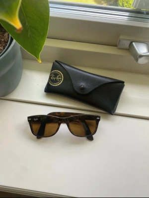 Rayban-vintage solglasögon  - Snygga Ray-Ban solglasögon i en liten mindre model med brunmelerad båge och bruna glas. Klassisk fyrkantig form och ikonisk logga på linsen. Kommer med original svart fodral. Perfekta för soliga dagar och en cool look. 