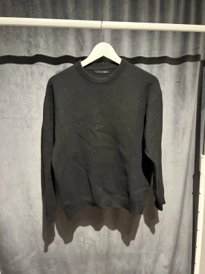 Svart stickad tröja från Zara - En enkel och stilren svart stickad tröja från Zara. Tröjan har rund halsringning och ribbade muddar vid hals, ärmslut och nederkant. Perfekt basplagg för lager på lager och funkar till det mesta.