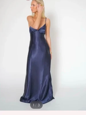 Marinblå långklänning Sophie - Säljer en elegant marinblå långklänning från By Stina, modell Sophie. Klänningen har en slät och glansig yta som ger en lyxig känsla. Perfekt för dig som vill ha en stilren och tidlös look.