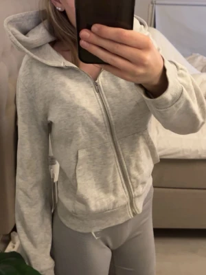 Ljusgrå zip hoodie med huva - Säljer en ljusgrå hoodie med dragkedja och huva. Hoodien har två fickor framtill och ribbade muddar vid ärmslut och nederkant.En liten liten fläck som man inte tänker på (sista bilden)