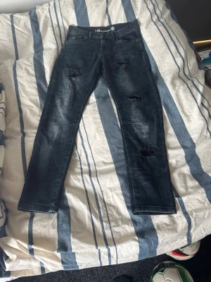 Svarta slitna jeans från LAB Industries - Säljer ett par svarta jeans från LAB Industries med slitningar på låren och knäna. Riktigt skön tvätt och är storlek 140