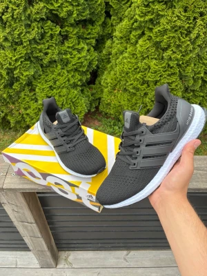 Adidas Ultraboost svarta sneakers - Svarta Adidas Ultraboost sneakers med stickad ovandel i mesh, vita Boost-sulor och svarta detaljer. Klassisk tre-randig design på sidorna och Continental-gummisula undertill för extra grepp. Perfekta för dig som gillar sportig och stilren look.