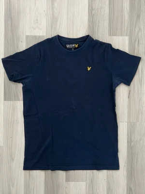 Mörkblå t-shirt från Lyle & Scott - Snygg mörkblå t-shirt från Lyle & Scott med klassisk gul logga broderad på bröstet. T-shirten har rund halsringning och korta ärmar. Tillverkad i mjuk bomull för skön känsla hela dagen.