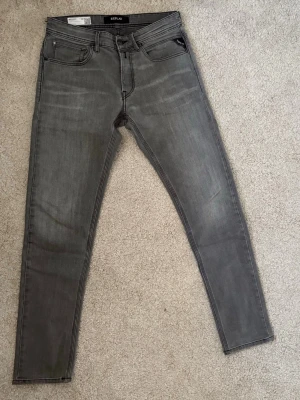 Replay jeans  - Säljer ett par grå slim fit jeans från Replay med klassisk femficksmodell och svarta detaljer. Jeansen har en snygg tvättad look och raka ben med smal passform. Materialet är mjukt och stretchigt för extra komfort.
