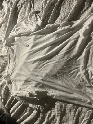 Vit t-shirt från Ralph Lauren - Klassisk vit t-shirt från Ralph Lauren med den ikoniska broderade loggan i mörkblått på bröstet. T-shirten har rund hals och korta ärmar, tillverkad i mjuk bomull för en skön och avslappnad stil.