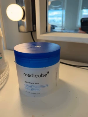 Medikube Zero Pore Pad toner - Zero Pore Pad toner från Medicube i en rund plastburk med blått lock. Innehåller tunna, vita pads indränkta i toner med AHA, BHA, panthenol och allantoin. Perfekt för att fräscha upp huden och minimera porer.