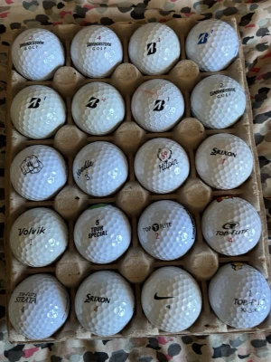 Blandade golfbollar i kartong - En kartong med 20 stycken vita golfbollar från olika märken som Bridgestone, Srixon, Top Flite, Volvik, Nike och Strata. Bollarna har klassisk rund form och är tillverkade i slitstarkt material. Perfekt för dig som vill fylla på golfbagen med olika bollar.
