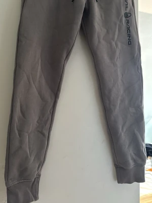 Grått Sail Racing klädesset - Snygga gråa mjukisbyxor och grå hoodie från Sail Racing med logga tryckt längs ena benet. Byxorna har muddar vid bensluten och dragsko i midjan för skön passform. Perfekta för en avslappnad stil och riktigt bekväma. Sitter bäst på folk runt 170-175