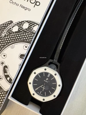Swatch x AP Ocho Negro klocka - Säljer en Swatch x Audemars Piguet Ocho Negro klocka med svart urtavla och vit ram. Klockan har en oktagonal form, svarta detaljer och svart band med vit söm. En riktigt snygg accessoar för dig som gillar ikonisk design.