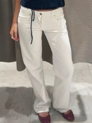 Vita raka jeans med hög midja - Säljer ett par vita jeans med rak passform och hög midja. Jeansen har klassisk femficksdesign, bälteshällor och stängs med knapp och dragkedja. Perfekta för en clean och fräsch look.