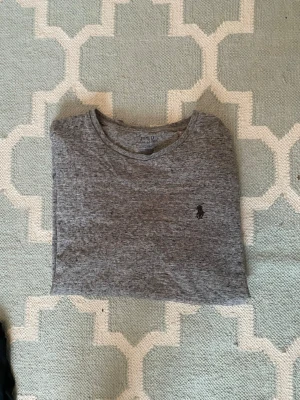 Grå t-shirt från Polo Ralph Lauren - Snygg gråmelerad t-shirt från Polo Ralph Lauren med klassisk rund hals och diskret logga broderad på bröstet. Perfekt basic-plagg som funkar till allt och har en skön passform. Tillverkad i mjuk bomull för maximal komfort.