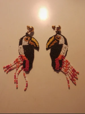 Färgglada pärlörhängen med tukanmotiv - Unikai örhängen i form av t t entries med tukanmotiv, handgjorda av protocols i svart, vitt, gult, orange och rosa. tallar och fransar av pärlor ger en cool och lekfull look. Perfekta för dig som vill sticka ut med accessoarer som syns.