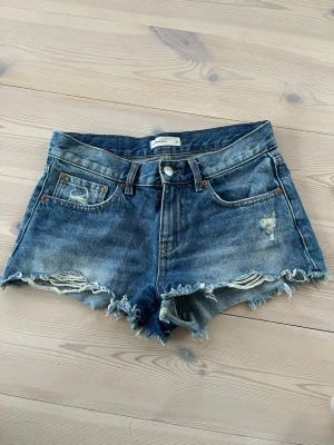 Blå jeansshorts - Säljer ett par blå jeansshorts från Gina Tricot Perfect Jeans med fransig rå kant och slitna kanter. Perfekta till sommaren 