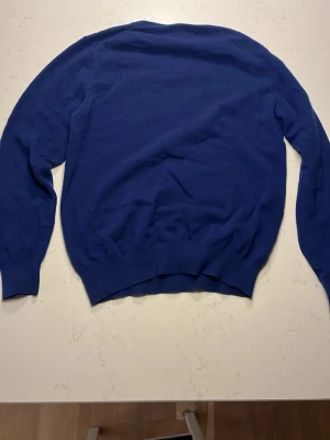 Mörkblå stickad tröja - En enkel och stilren mörkblå stickad tröja med rund halsringning och långa ärmar. Tröjan har ribbade muddar vid ärmslut och nederkant, vilket ger en klassisk look. Perfekt att matcha med jeans eller kjol för en avslappnad stil.