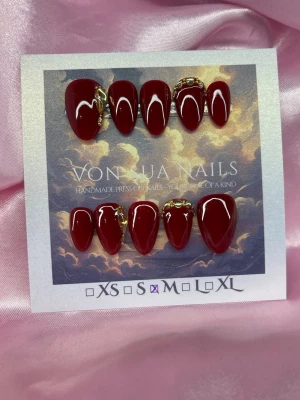 Scarlet (M);Short Almond - Snygga handgjorda press-on naglar i en djup vinröd färg med glansig finish. Några naglar har dekorativa gulddetaljer som ger en lyxig känsla. Formen är kort almond och storleken är M: 16 mm, 12 mm, 12,5 mm, 11,5 mm, 10 mm. Perfekta för dig som vill ha ett statement på naglarna.