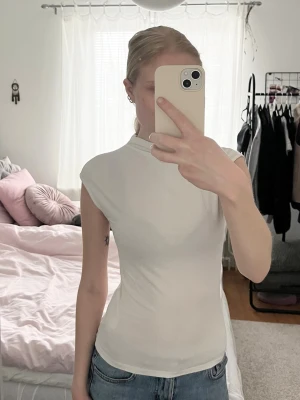 Vit tight topp från Gina Tricot - Säljer en vit topp med liten krage från Gina Tricot. Modellen är tight med korta ärmar och hals. 