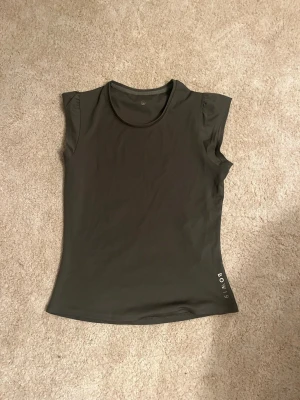 Mörkgrön topp  - Snygg mörkgrön topp med soprena linjer. Modellen är ärmlös med rund halsringning och lätt figurnära passform. Materialet känns mjukt och stretchigt, perfekt för en aktiv livsstil.