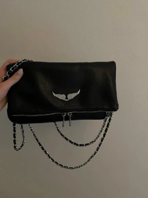 Zadig voltaire väska  - Snygg svat kuvertväska med silverfärgad kedja och dragkedjedetaljer. Vä strassving flärp ofram och extra fack med dragkedja backward. Gjord i konstläder vithäftig struktur. Perfekt accessoar dec till en trendig outfit.