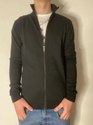 Svart ziptröja från Selected Homme - Snygg svart ziptröja från Selected Homme med hög krage och hel dragkedja framtill. Tröjan har en stilren design, långa ärmar och ribbade muddar vid ärmslut och nederkant. Perfekt att bära över en t-shirt för en clean look.