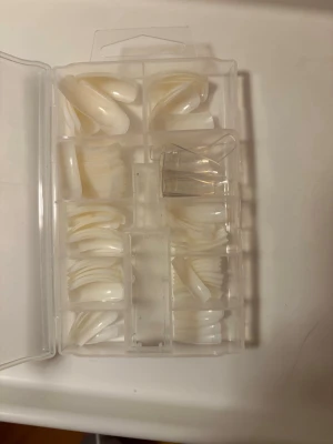 Mixade press-on naglar i box - Säljer ett set med press-on naglar i olika storlekar, levereras i en praktisk plastbox. Naglarna är i en naturlig, mjölkvit färg och har en klassisk oval form. Perfekta för att skapa egna designer hemma. Materialet är tålig plast.