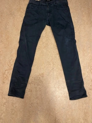 Svarta Replay Hyperflex jeans - Säljer ett par svarta Replay Hyperflex jeans med klassisk femficksmodell och smal passform. Jeansen har stretchigt material som ger extra komfort och rörelsefrihet. Perfekta för dig som gillar en stilren och modern look.