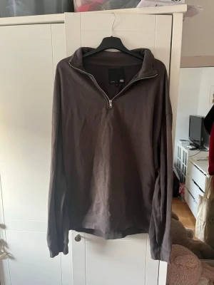 Mörkbrun halvzip tröja från lager 157 - Säljer en mörkbrun långärmad tröja från lager 157 med halv dragkedja och hög krage. Tröjan har avslappnad passform och är gjord i mjukt bomullsmaterial. Perfekt för en chill och stilren look.