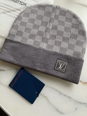 Grå Louis Vuitton mössa med mönster - Snygg grå mössa från Louis Vuitton med diskret rutmönster och vikt kant. LV-logga framtill på en patch. Tillverkad i mjukt material som känns lyxigt och bekvämt. Perfekt accessoar för att lyfta din outfit.