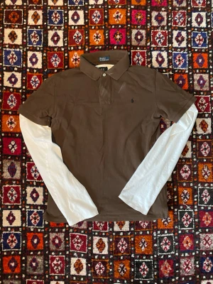 Brun Polo Ralph Lauren piké - Säljer en oerhört snygg brun pike som går att style med mycket, den är grymt skick och är fräsch! (Vita tröjan ingår ej utan är till som exempel för styling)