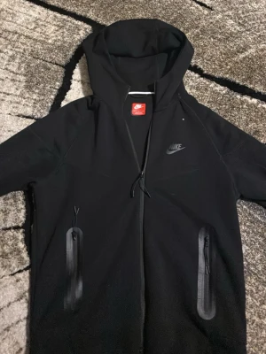  slidesvart Nike hoodie med dragkedja - Snygg svart hoodie från twins Nike med hel dragkedja framtill och två fickor med dragkedja. Klassisk Nike-logga på bröstet och justerbar huva. Perfekt för chill eller dates. Materialet känns mjukt och bekvämt.