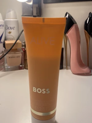 BOSS Alive hand & body lotion - En lyxig hand- och kroppslotion från BOSS Alive i en snygg persikofärgad tub med gulddetaljer. Lotionen är parfymdoftande och passar perfekt för att återfukta huden. Tuben rymmer 75 ml och har en modern, stilren design.