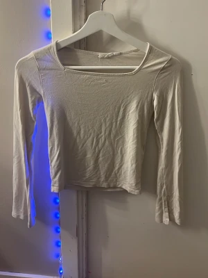 Ljusvit croppad långärmad topp - En enkel och stilren ljusvit croppad topp med lång ärm och br med slit ed, fyrkantig halsringning. Perfekt att matcha med jeans eller kjol för en clean look. Materialet är mjukt och stretchigt, troligtvis bomull eller en bomullsblandning.