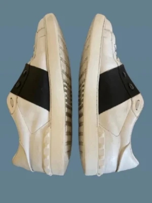 Valentino open sneakers - Snygga vita sneakers från Valentino med en bred svart läderdetalj över mitten. Klassisk låg modell med rund tå och vita snören. Skorna har en stilren och modern design, perfekt för dig som gillar exklusiva märken och streetstyle🙌| Självklart äkta men innersulan är bytt för bättre kvalitet🤝