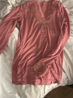 Rosa loungewear-tröja från Intimissimi - Mysig rosa loungewear-tröja från Intimissimi i ultralätt material med kashmir. Tröjan har långa ärmar och vacker spetsdetalj vid V-ringningen och ärmsluten. Perfekt för chill dagar hemma.