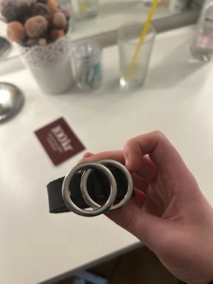 Svart lä stead bälte med dubbla sopringarres - 120 cm långt svart bälte i äkta läder med två silverfärgade ringar som spännene. Stilren och enkel design, perfekt för att lyfta vilken outfit som helst. Tillverkat i Sverige. Har gjort ett eget hål i skärpet så att den skulle kunna passa , men det syns inte.