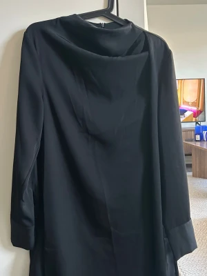 Svart enkel klänning  - Stilren svart klänning med trekvartsärm och lös passform. Klänningen har en mjuk, något glansig yta och en enkel, rak siluett.🖤