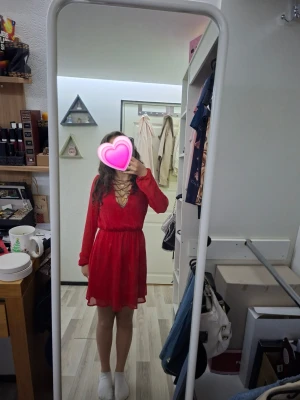 Röd klänning - Snygg röd kort klänning med omlottdesign och djup v-ringning med snörningsdetalj framtill. Långa ärmar och markerad midja.Tyvär ett litet hål vid höger arm märks knappt men bra att veta.