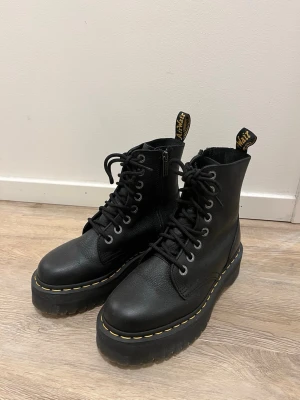 Svarta Dr. Martens Jadon kängor - Säljer ett par svarta Dr. Martens Jadon kängor i läder med grov platåsula och klassiska gula sömmar. Kängorna har snörning, dragkedja på sidan och Dr. Martens logga på trailern bak. Modellen är Dr martens jadon iii unisex. Storlek 38. Använda 1 gång. Originalpris 2495kr. Säljer för 1200kr  