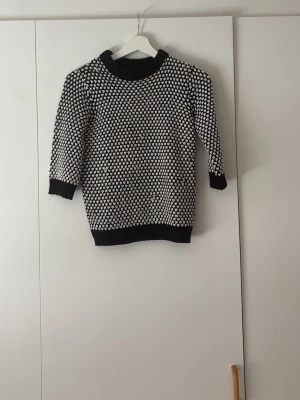 Svartvit stickad tröja med mönster - Säljer en svartvit stickad tröja med tätt prickigt mönster. Tröjan har rund halsringning, ribbade muddar och nederkant samt trekvartsärmar. Perfekt för dig som gillar klassiska färger och enkel design.