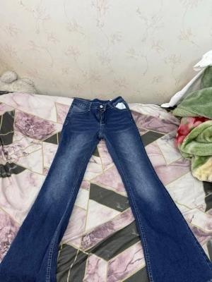 Blå utsvängda jeans med låg  midja - Säljer ett par blå jeans med utsvängda ben och hög midja. Jeansen har klassisk femficksdesign och snygga slitningar framtill. Perfekta för dig som gillar retrostil och vill ha ett par bekväma och trendiga jeans i garderoben. 