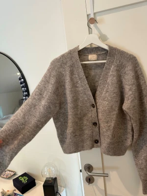 H&M stickad kofta - Mysig gråmelerad kofta med v-ringning och tre mörka knappar framtill. Koftan är gjord i en MOHAIR/WOOL blanding 