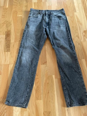 Grå raka jeans från Levi's 551z - Klassiska grå jeans från Levi's med rak passform och fem fickor. Jeansen har en vintage tvätt och är tillverkade i slitstark denim. Perfekta för en avslappnad och trendig look.