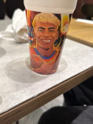 McDonald's samlarmugg med lamine yamal - Cool samlarmugg från McDonald's med färgglatt fotbollsmotiv. Muggen är i plast och har illustrationer av en fotbollsspelare i röd tröja och blå shorts, omgiven av eld och bollar. Perfekt för dig som gillar sportiga samlarprylar eller vill ha en unik dryckesbägare.