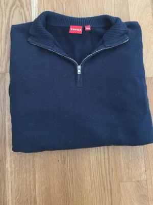 Mörkblå zip-tröja från RYVLS - En stilren mörkblå tröja från RYVLS med halvzip och ribbad krage. Perfekt för dig som gillar en enkel och klassisk look. Tröjan har lång ärm och är gjord i mjukt material som känns skönt mot huden.