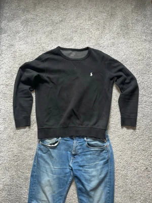 Svart sweatshirt från Polo Ralph Lauren - Klassisk svart sweatshirt från Polo Ralph Lauren med rund halsringning och den ikoniska vita polospelaren broderad på bröstet. Storlek small, mycket bra skick!