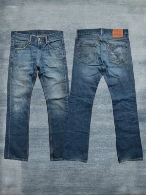 Levi's blå raka jeans med bootcut - Klassiska blå jeans från Levi's med rak passform och fem fickor. Jeansen har slitningar och en snygg tvättad look, samt den ikoniska läderpatchen bak i midjan. Tillverkade i slitstark denim med metallknappar och nitar. Dessutom är jeansen bootcut! Och storlek 30/32, Hör av er om frågor!