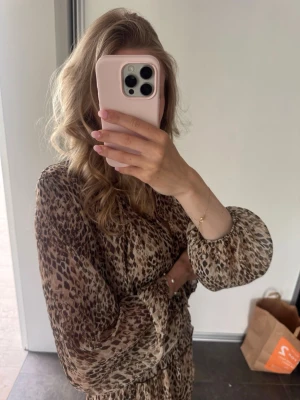 Leopardmönstrad klänning med volang - Säljer en leopardmönstrad klänning med långärmade, luftiga ärmar och volangdetaljer. Klänningen har en avslappnad passform och resår i midjan för en snygg siluett. Perfekt för dig som gillar djurmönster och trendiga detaljer. Priset kan diskuteras 