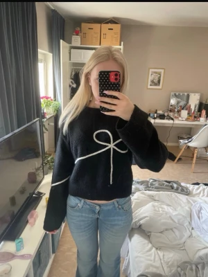 Svart stickad tröja Divided H&M - Säljer en svart stickad tröja från Divided H&M med en vit rosett framtill. Tröjan har en avslappnad passform, långa ärmar och ribbade muddar. Perfekt för dig som gillar en trendig och mysig look.